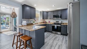 A modern kitchen with dark grey cabinets, a granite countertop, stainless steel appliances, and a large island with bar stools. - Wet Feet Retreat Waterfront-Manatees, Kayaks, SUPs (Spring Hill)