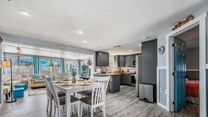 A modern kitchen with dark cabinets, a stainless steel refrigerator, and a dining area with a white table and chairs. - Wet Feet Retreat Waterfront-Manatees, Kayaks, SUPs (Spring Hill)