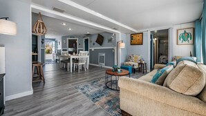 A spacious living area with a dining table, sofa, and a kitchen in the background. - Wet Feet Retreat Waterfront-Manatees, Kayaks, SUPs (Spring Hill)