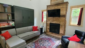 A cozy living room with a sofa, a black armchair, a fireplace, and a bookshelf with board games.