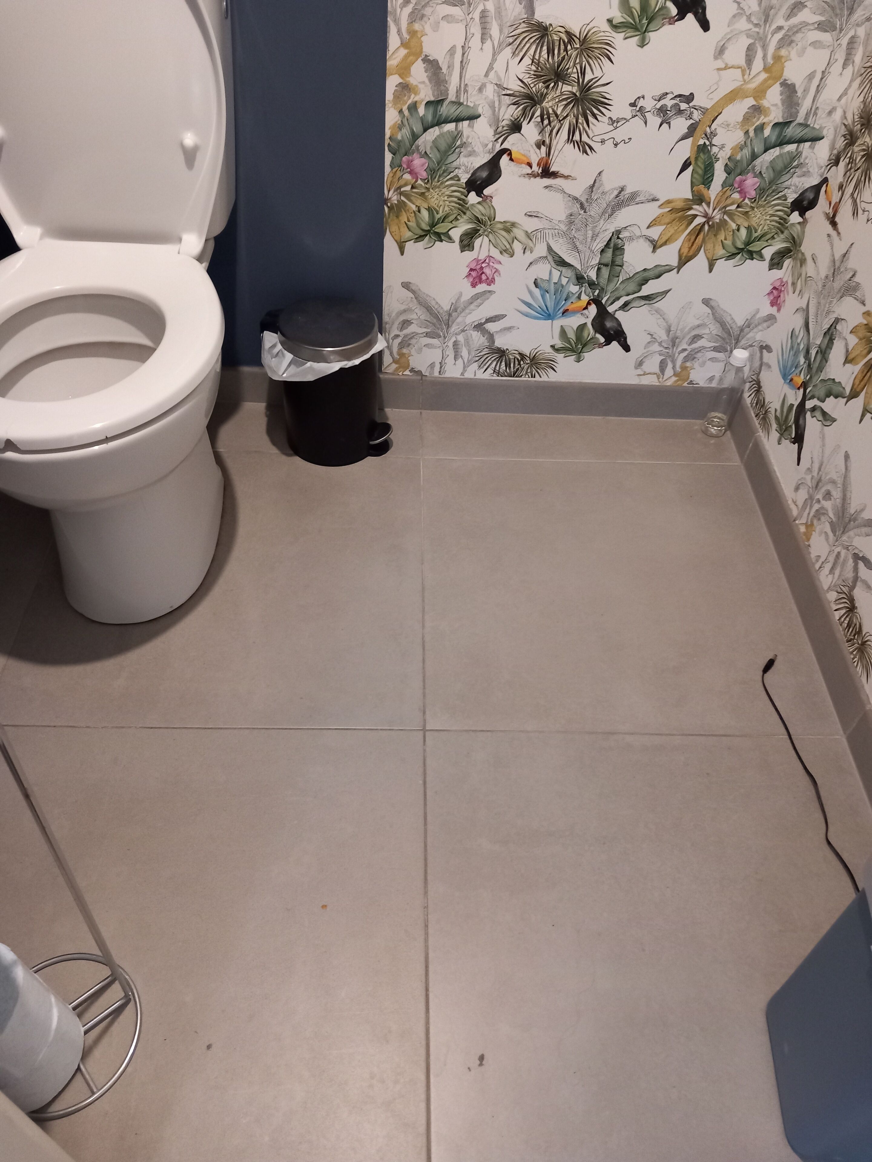 A bathroom with a toilet, a trash bin, and a tiled floor.