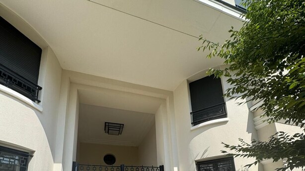 A building entrance with a black gate, white walls, and a small window above the door.