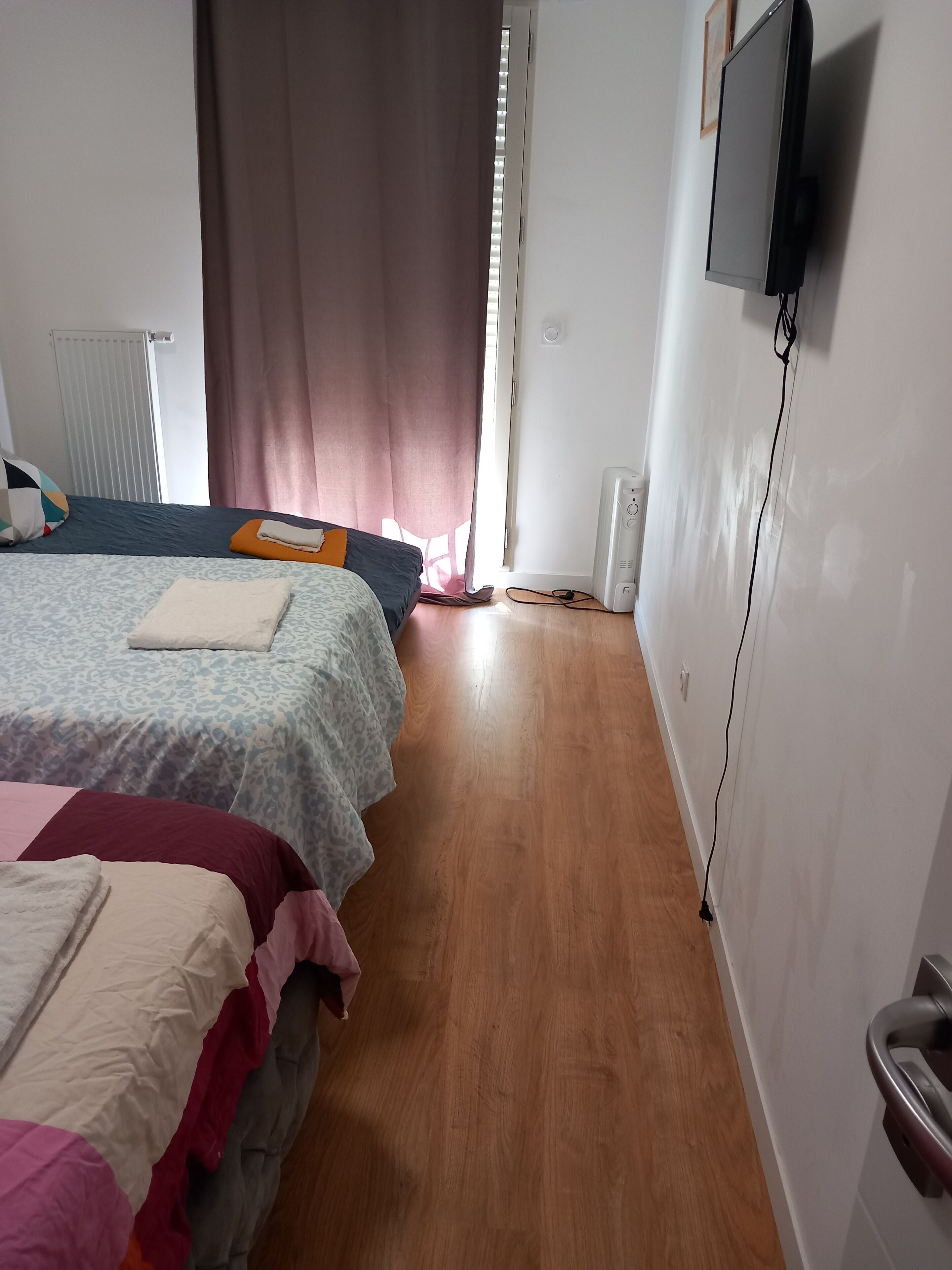 Een slaapkamer met twee bedden, een aan de muur bevestigde televisie en een radiator.