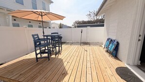 Una terraza de madera con una mesa, sillas, un paraguas y una valla blanca.