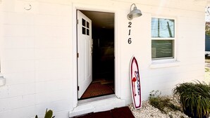 Un edificio blanco con el número 216 en la puerta, un letrero de bienvenida y una decoración con una tabla de surf.