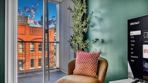Une chambre moderne dotée d’une grande fenêtre, d’une plante en pot, d’un fauteuil en cuir et d’un téléviseur à écran plat affichant un menu.