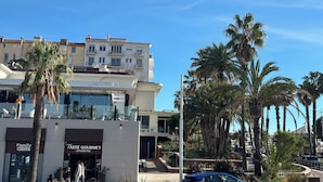 A building with a modern design, featuring a glass facade and a ground floor with a 'Family Game' and 'Taste Gourmet' shop. - Right in the town center, 5m from the beach on foot and 2m from the SNCF train station (Saint-Raphaël)