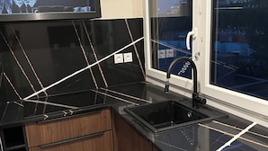 A modern kitchen with a black countertop, wooden cabinets, a stainless steel sink, and a window with a view of buildings. - Right in the town center, 5m from the beach on foot and 2m from the SNCF train station (Saint-Raphaël)