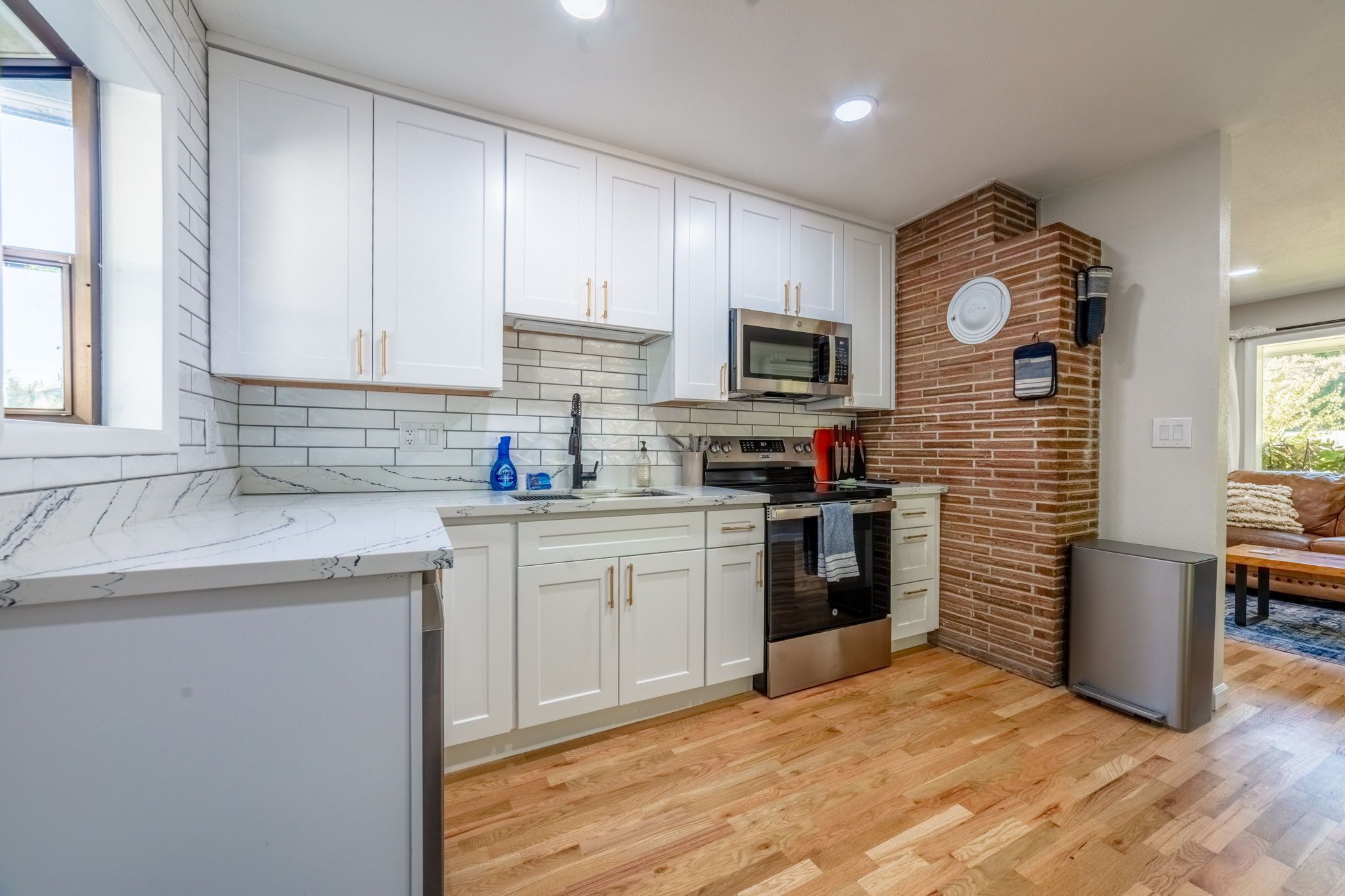 A modern kitchen with white cabinets, a built-in microwave, and a brick accent wall.