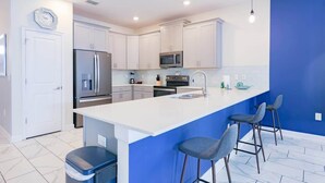 A modern kitchen with white cabinets, a stainless steel refrigerator, a microwave, and a blue accent wall. - 8BR Golf Resort Villa/Private Pool+Theater at home (Four Corners)