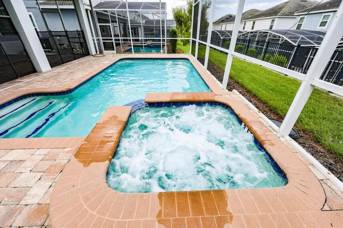 En swimmingpool med et spa, omgivet af et hvidt hegn og en flisegul terrasse.