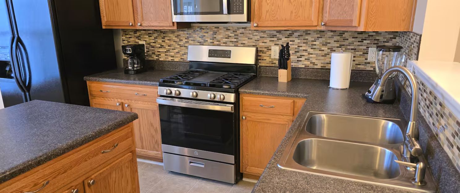 A kitchen with a Galaxy S24 Ultra stove, wooden cabinets, a stainless steel sink, and a coffee maker.