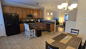 Una cocina moderna con una isla central, armarios de madera, un refrigerador negro y un comedor con mesa y sillas.