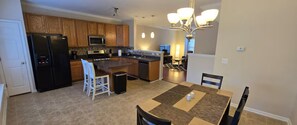 A modern kitchen with a central island, wooden cabinets, a black refrigerator, and a dining area with a table and chairs. - NEW! Ready for Families and Business Travelers (Raleigh)