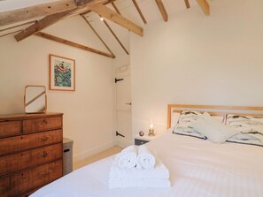 A bedroom with a wooden dresser, a bed with white linens, a framed picture on the wall, and a small bedside table with a lamp. - The Well House (Lyme Regis)