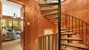 A wooden interior with a spiral staircase, a bed, and a view of greenery outside.