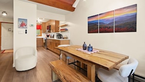 A modern kitchen with wooden cabinets, a dining table with benches, and a wall-mounted painting.