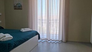 A bedroom with a bed, a window with sheer curtains, and a small painting on the wall.