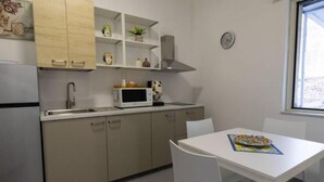 A small kitchenette with a microwave, sink, and cabinets. There is a white table with chairs and a window with a view.