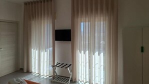 A room with large windows, a flat-screen TV mounted on the wall, and a metal drying rack near the windows.