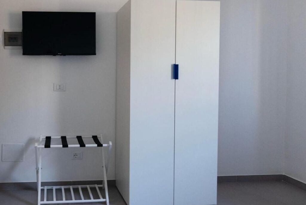Ein Zimmer mit einem weißen Kleiderschrank, einem Wand-Fernseher und einem weißen Wäscheständer.