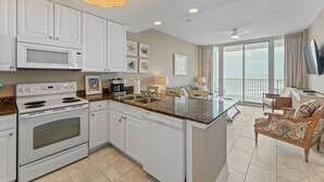 A kitchen with white cabinets, a microwave, and a stove. There is a dining area with a table and chairs, and a balcony with a view. - Lighthouse 603, Owner Managed. Beautiful Beachfront Condo (Gulf Shores)
