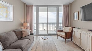 A modern living room with a sofa, armchair, coffee table, and a TV on a cabinet. - Lighthouse 603, Owner Managed. Beautiful Beachfront Condo (Gulf Shores)