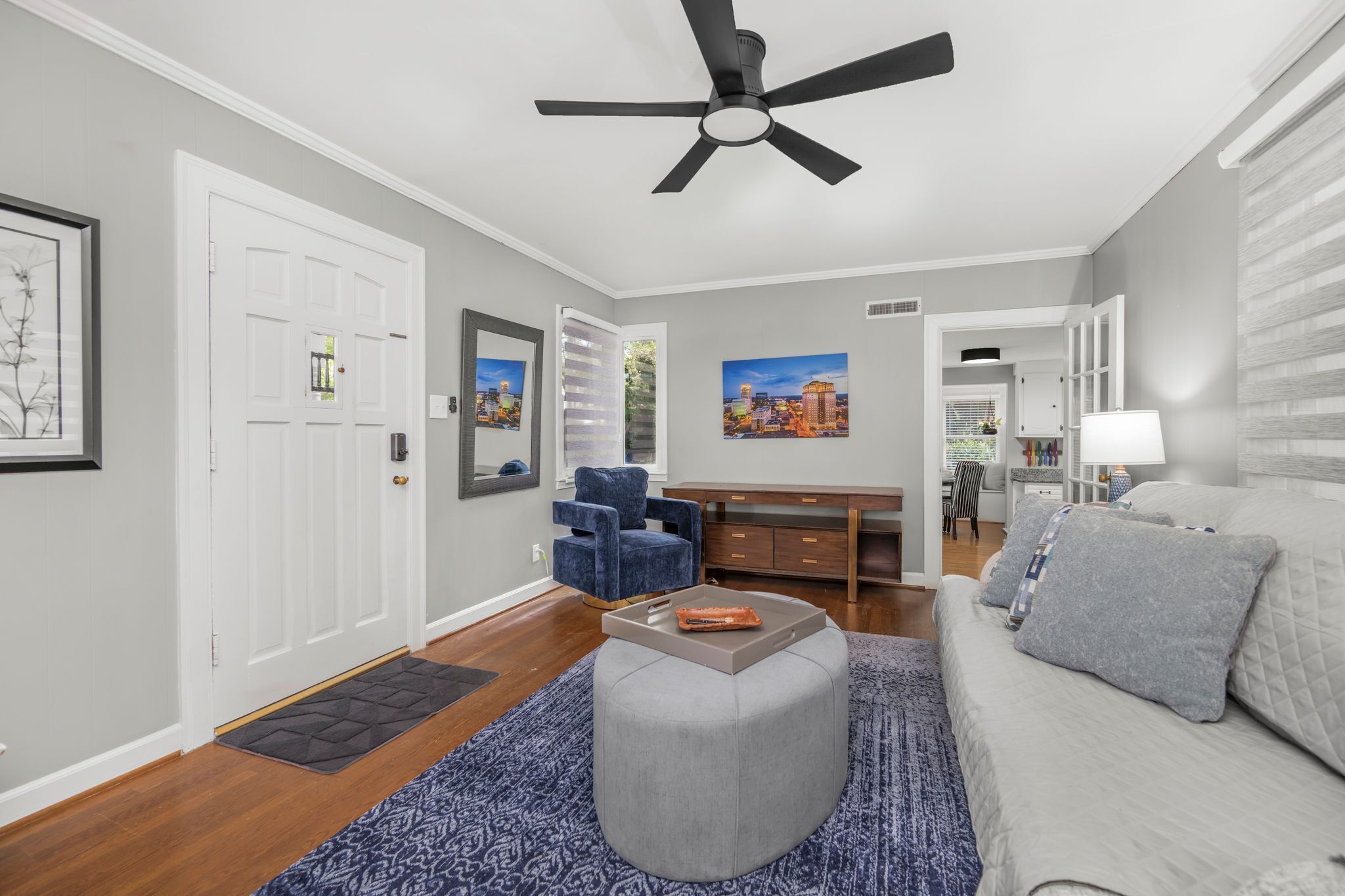 A modern living room with a grey sofa, a blue armchair, a wooden desk, and a ceiling fan.