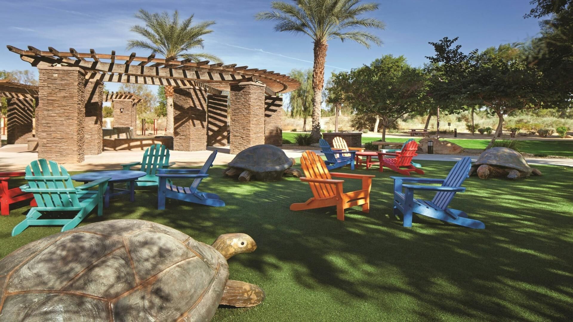 A patio area with Adirondack chairs, a pergola, and a turtle on artificial grass.