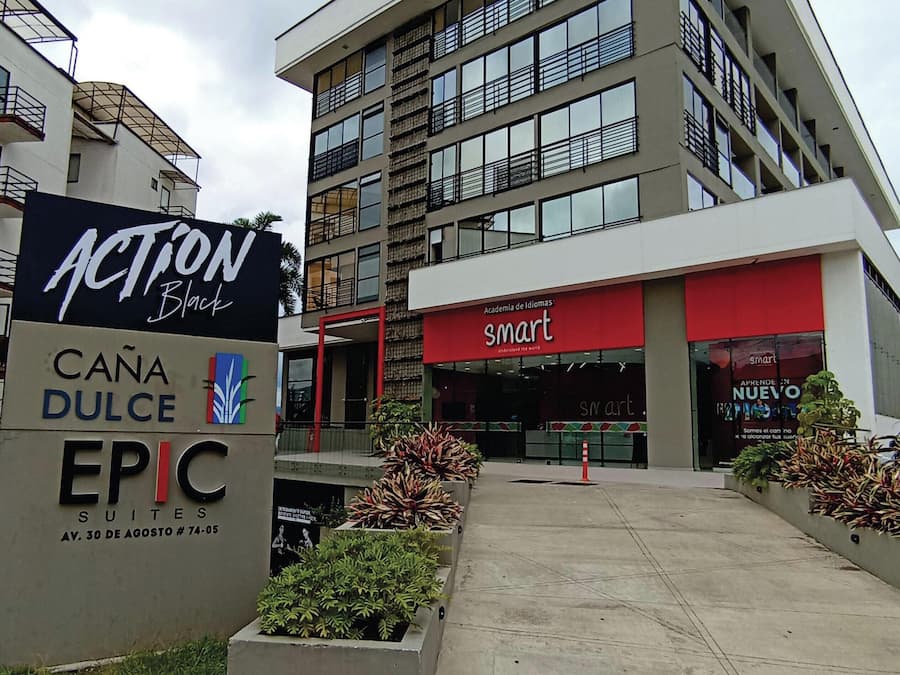 A multi-story building with a sign for 'Action Black' on the left and 'smart' on the right. There are planters with greenery in front.