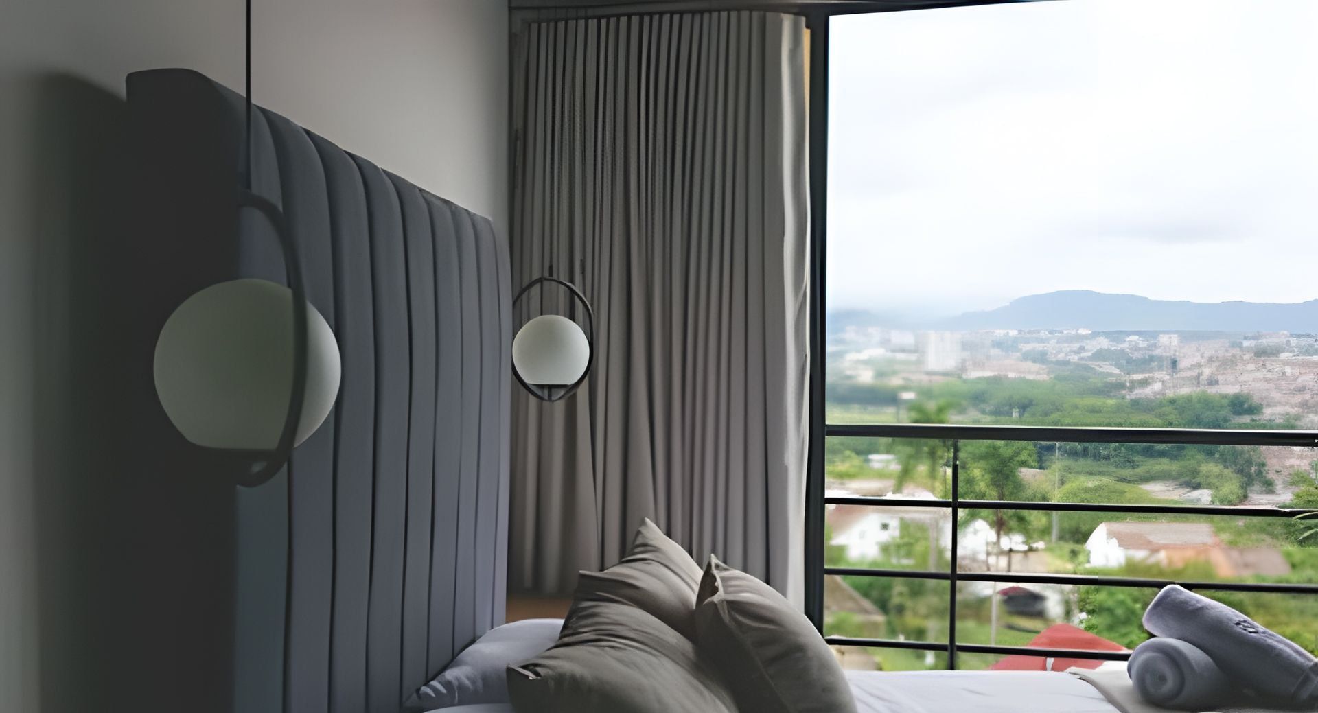 A modern bedroom with a large window, a bed with multiple pillows, and a headboard with built-in lighting.