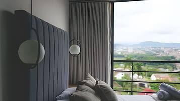 A modern bedroom with a large window, a bed with multiple pillows, and a headboard with built-in lighting.