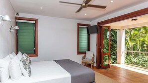 Une chambre à coucher comprenant un lit, une chaise, un ventilateur de plafond et un balcon avec vue sur la verdure.