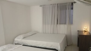 A bedroom with two single beds, a small desk with a lamp, and a window with sheer curtains.