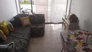A living room with a sofa, a dining table with a cat-themed tablecloth, and a view through a glass door.