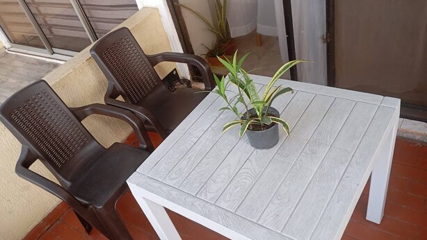 A patio with a white table and two dark chairs, a potted plant, and a sliding glass door.