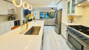 Een moderne keuken met een centraal eiland, roestvrijstalen apparatuur en hangende lampen.