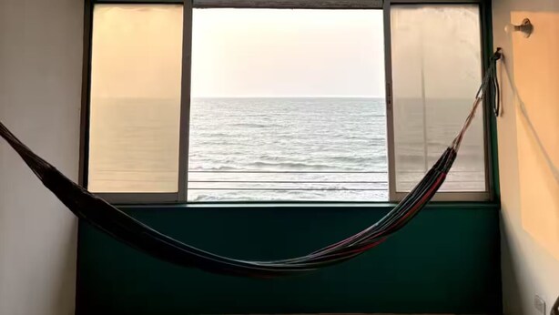 A room with a large window overlooking the sea, a hammock, and a green wall. - @casa_grace Nice apartment with ocean view (Cartagena de Indias)