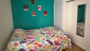 A bedroom with teal walls, a bed with colorful feather-patterned bedding, a small desk, and a door with a mirror. - @casa_grace Nice apartment with ocean view (Cartagena de Indias)