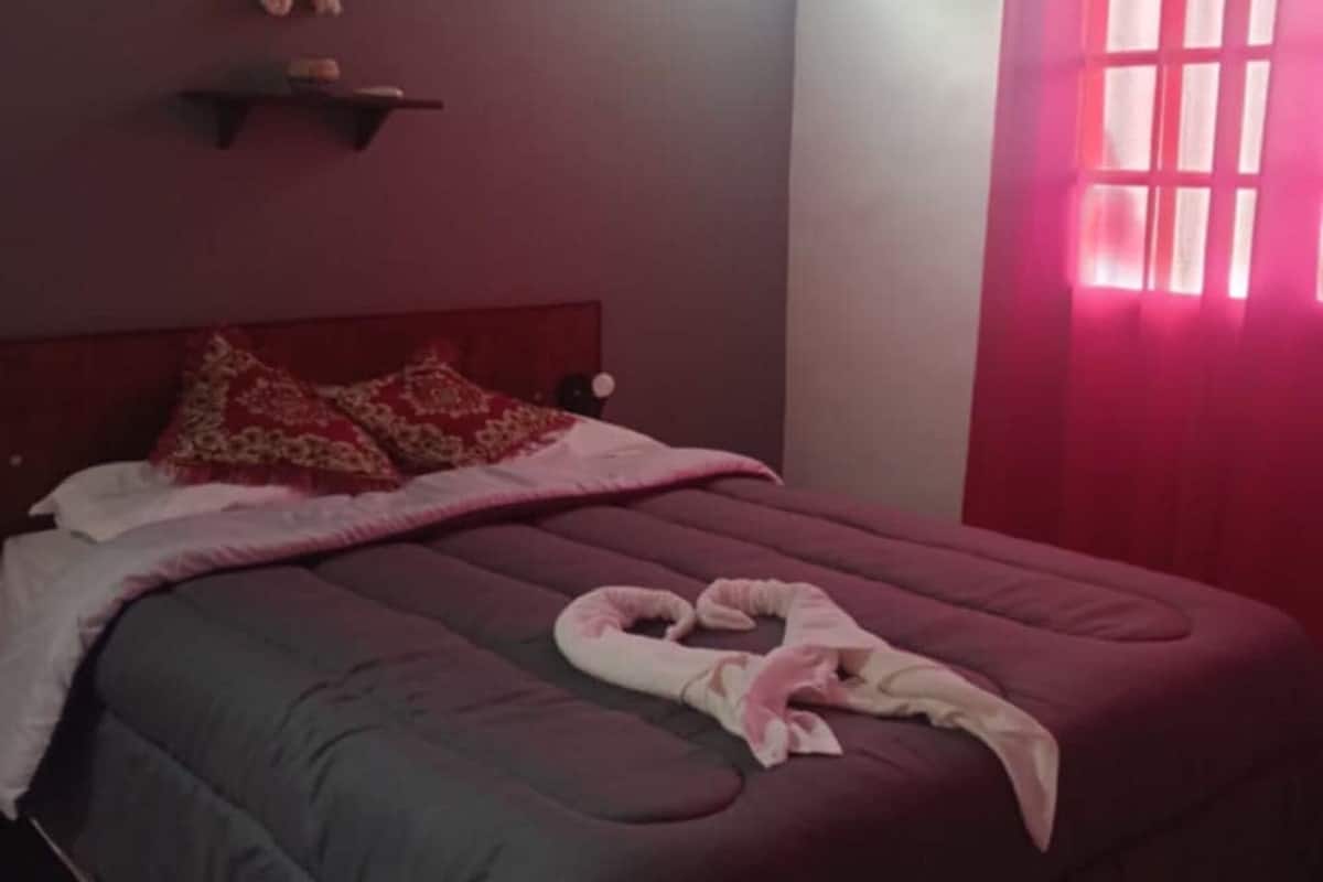 Un dormitorio con cama, almohadas, una lámpara colgante y una ventana con cortinas.