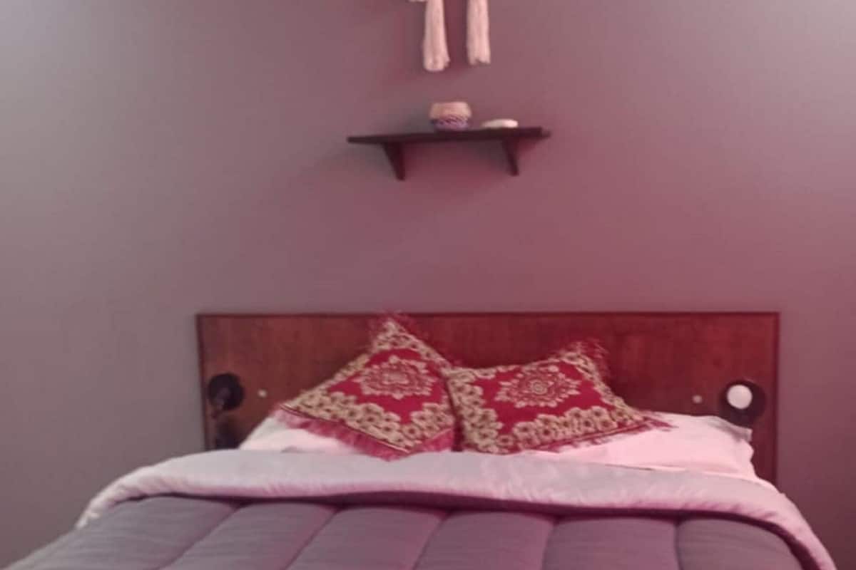 Una cama con cabecera, un adorno colgante en la pared y una toalla rosa sobre la cama.