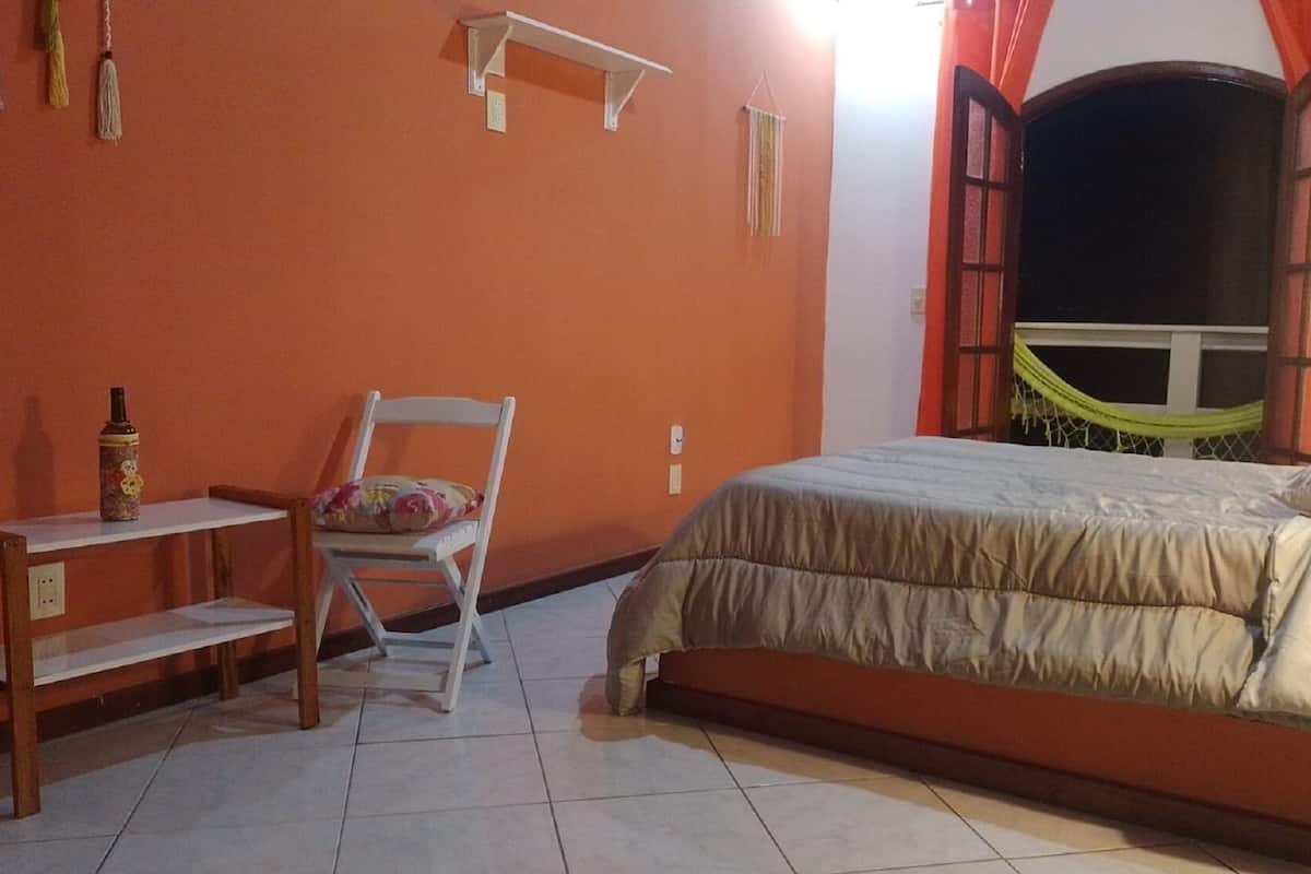 Un dormitorio con cama, una silla, un estante y una ventana con cortinas.