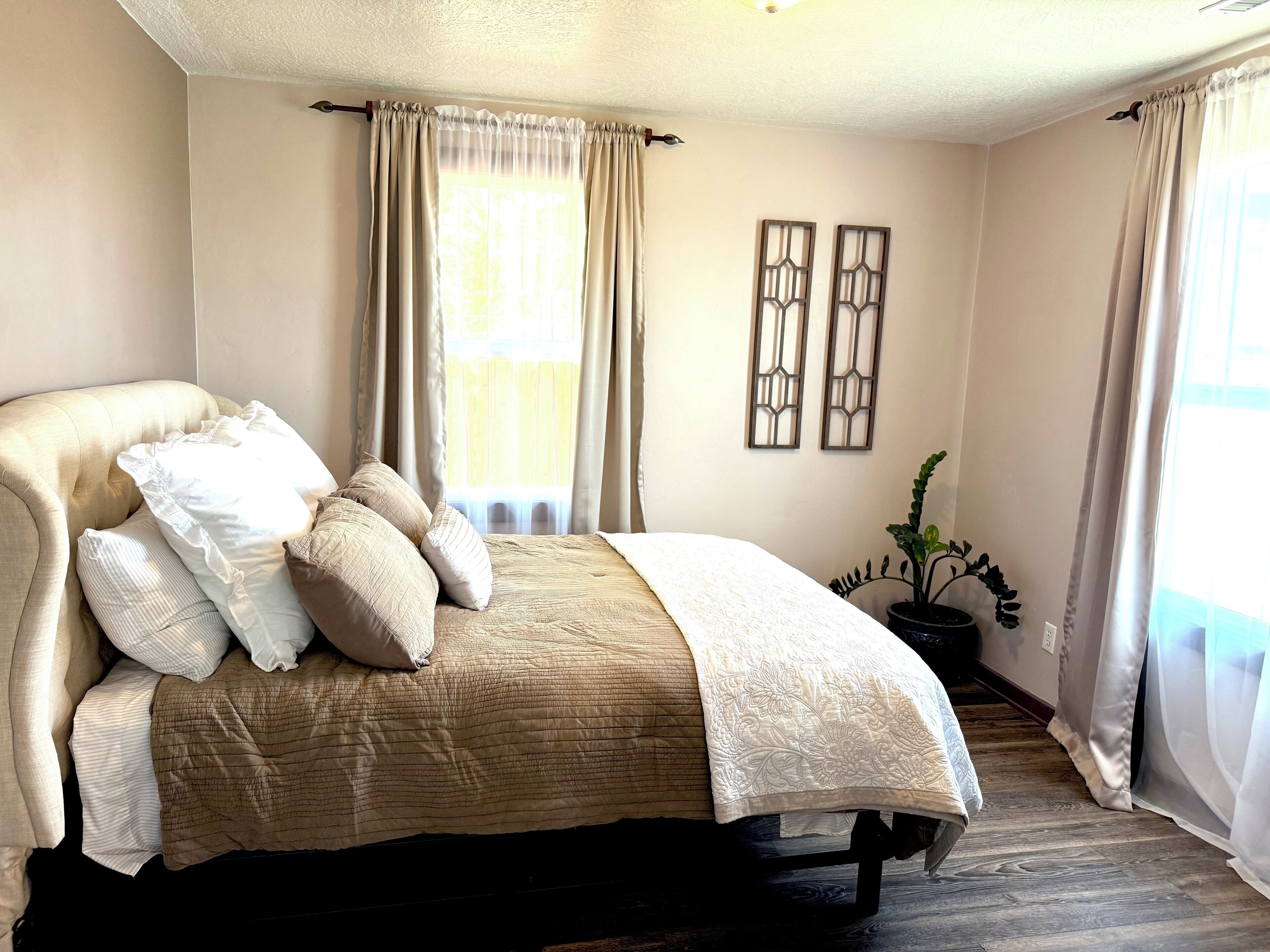 A bedroom with a bed, curtains, a potted plant, and two wall-mounted decorations.