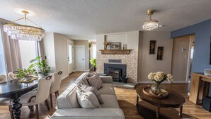 Ein geräumiges Wohnzimmer mit Kamin, ein Essbereich mit einer Chandelieber und eine moderne Küche im Hintergrund.