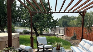 Eine Holzterrasse mit Gartenmöbeln, darunter Stühle und eine Sitzecke, unter einer Pergola.