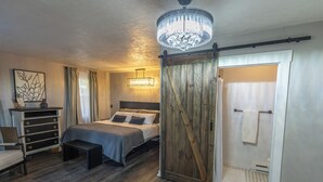 Ein Schlafzimmer mit Bett, Schminktisch, einer Bank, einer Kristallleuchtreiter und einer Holztür im Bauernhausstil.
