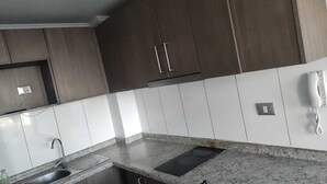 A kitchen with dark wooden cabinets, white tiles, a granite countertop, a sink, and a telephone. - Alojamientos On Santiago (Santiago)
