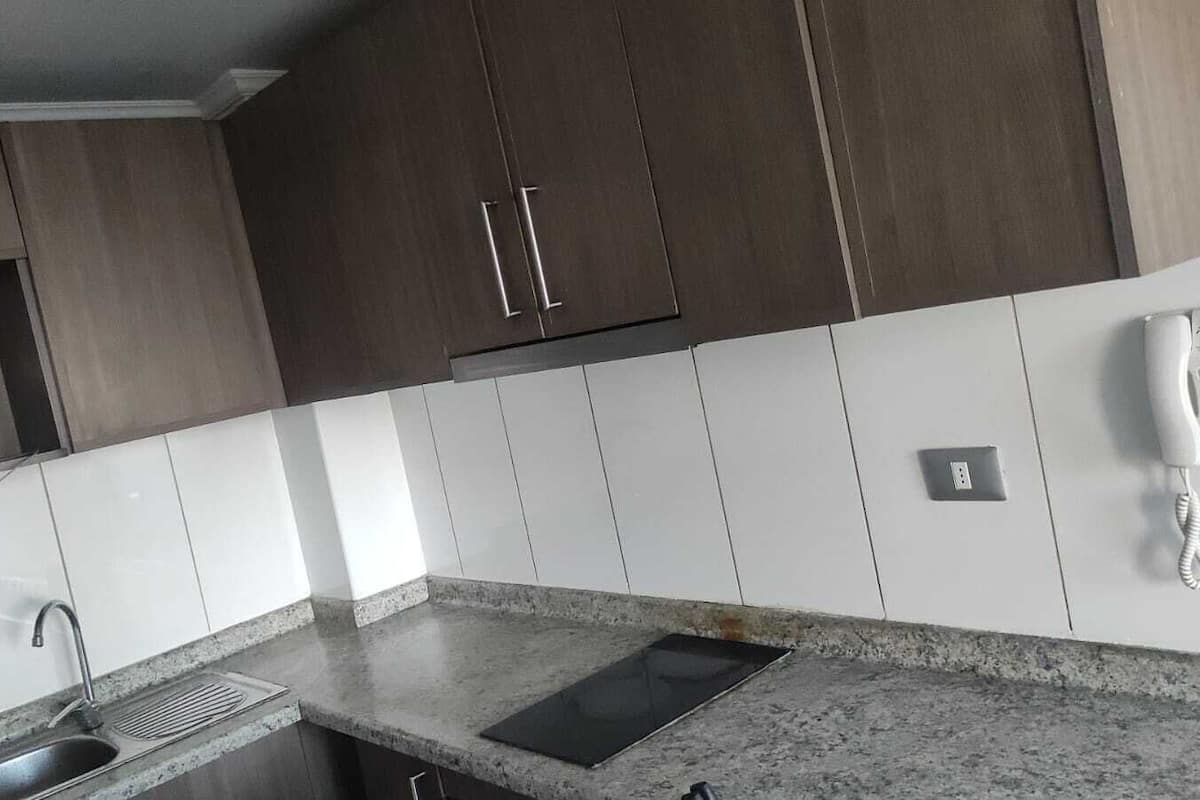 A kitchen with dark wooden cabinets, white tiles, a granite countertop, a sink, and a telephone.