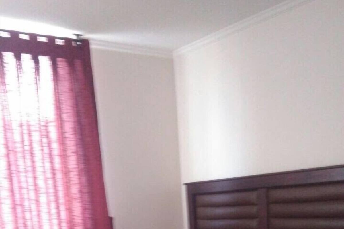 A room with a bed, a wooden headboard, a red curtain, and a small wooden dresser.