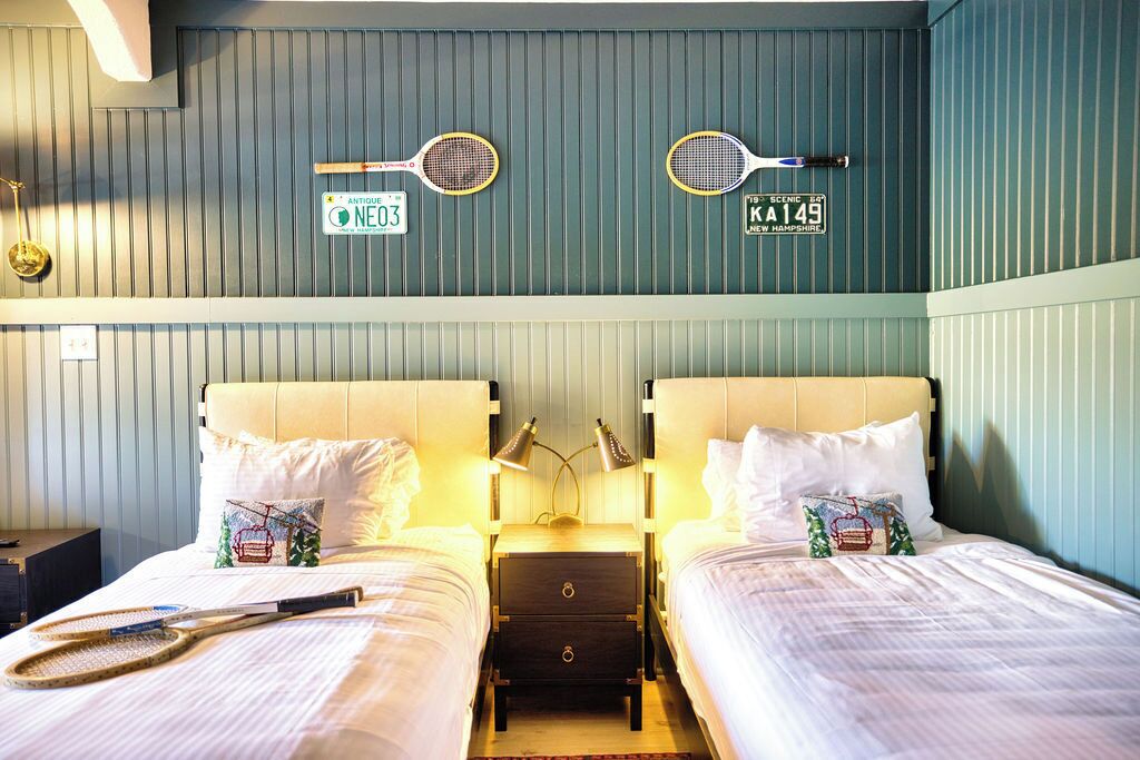 Une chambre d’hôtel avec deux lits, une table de chevet avec une lampe et deux raquettes de tennis accrochées au mur.